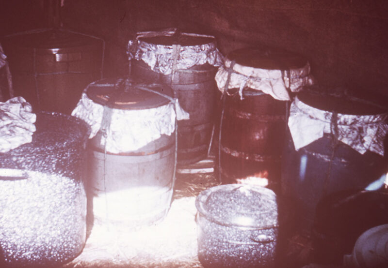 Several large metal barrels covered with cloth are standing in a dimly lit area. The barrels vary in size and color.