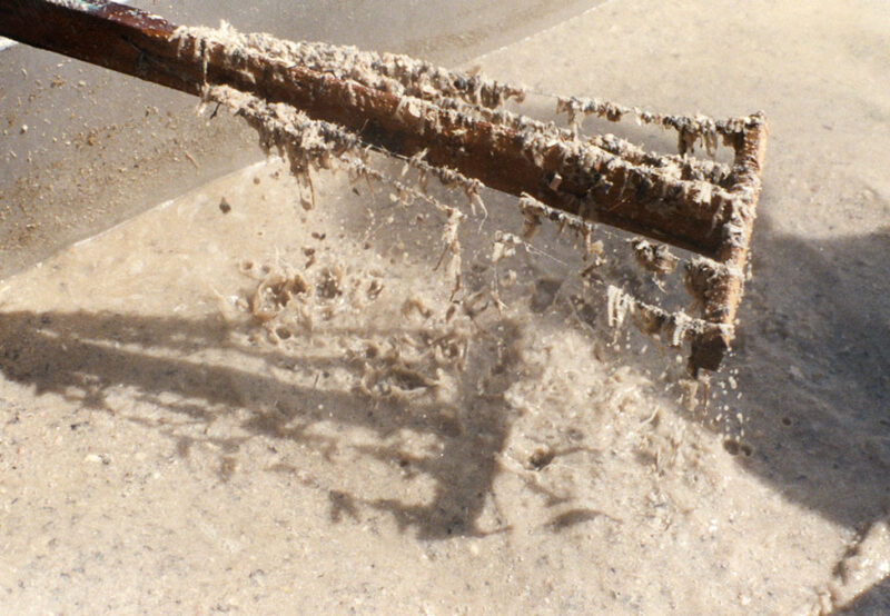 A close-up view of a rake covered in a thick layer of mud being cleaned in water.